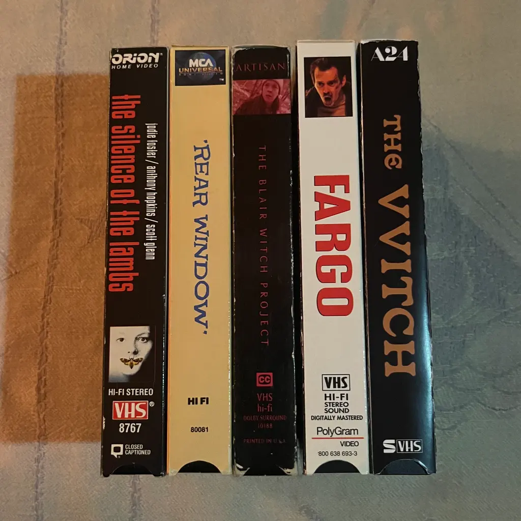 Five VHS video cassettes standing upright showing spines with titles including “Silence of the Lambs”, “Fargo”, and “Vvitch”.